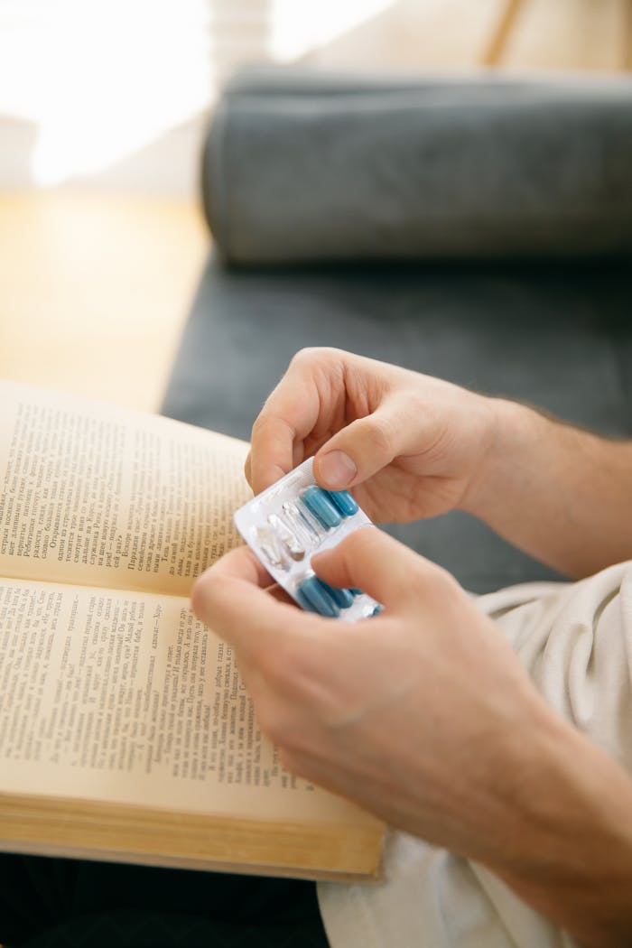 Close-up of hands holding medicine blister while reading a book indoors.